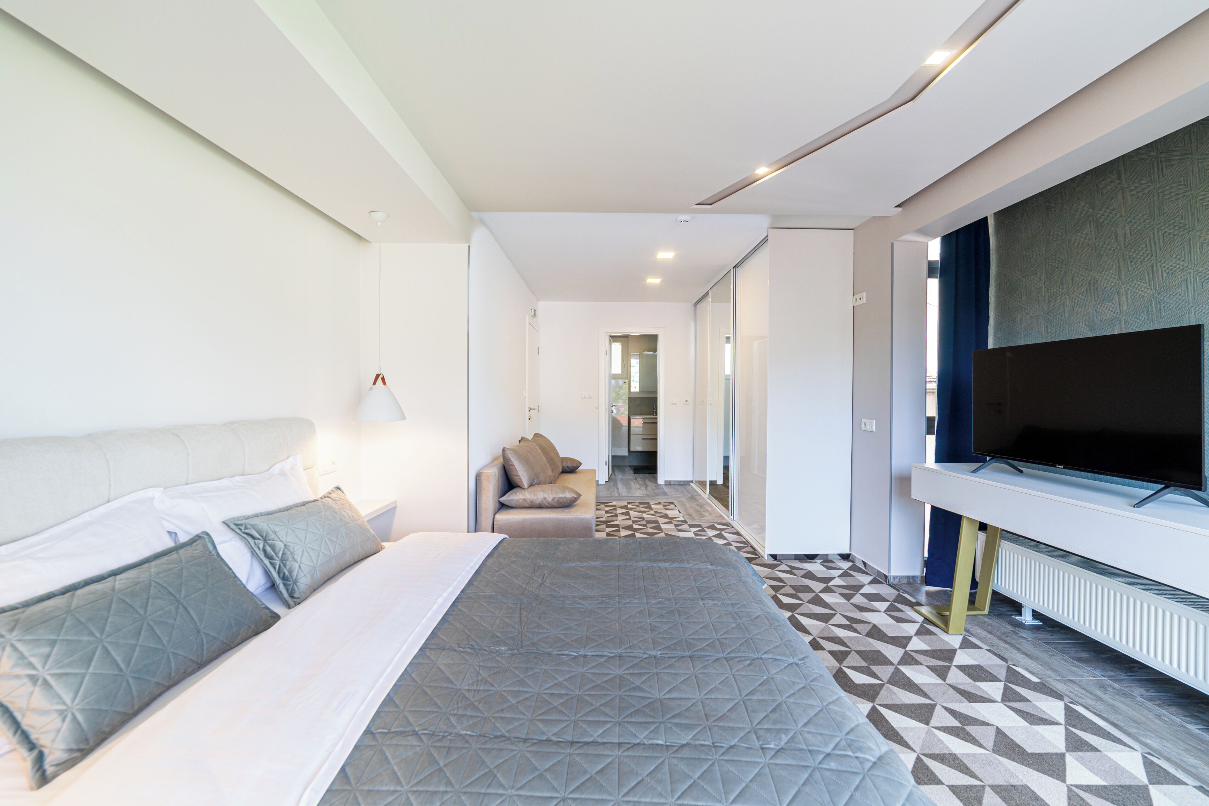 Una habitación de hotel moderna con una cama, un sofá, un televisor y un piso con diseño.