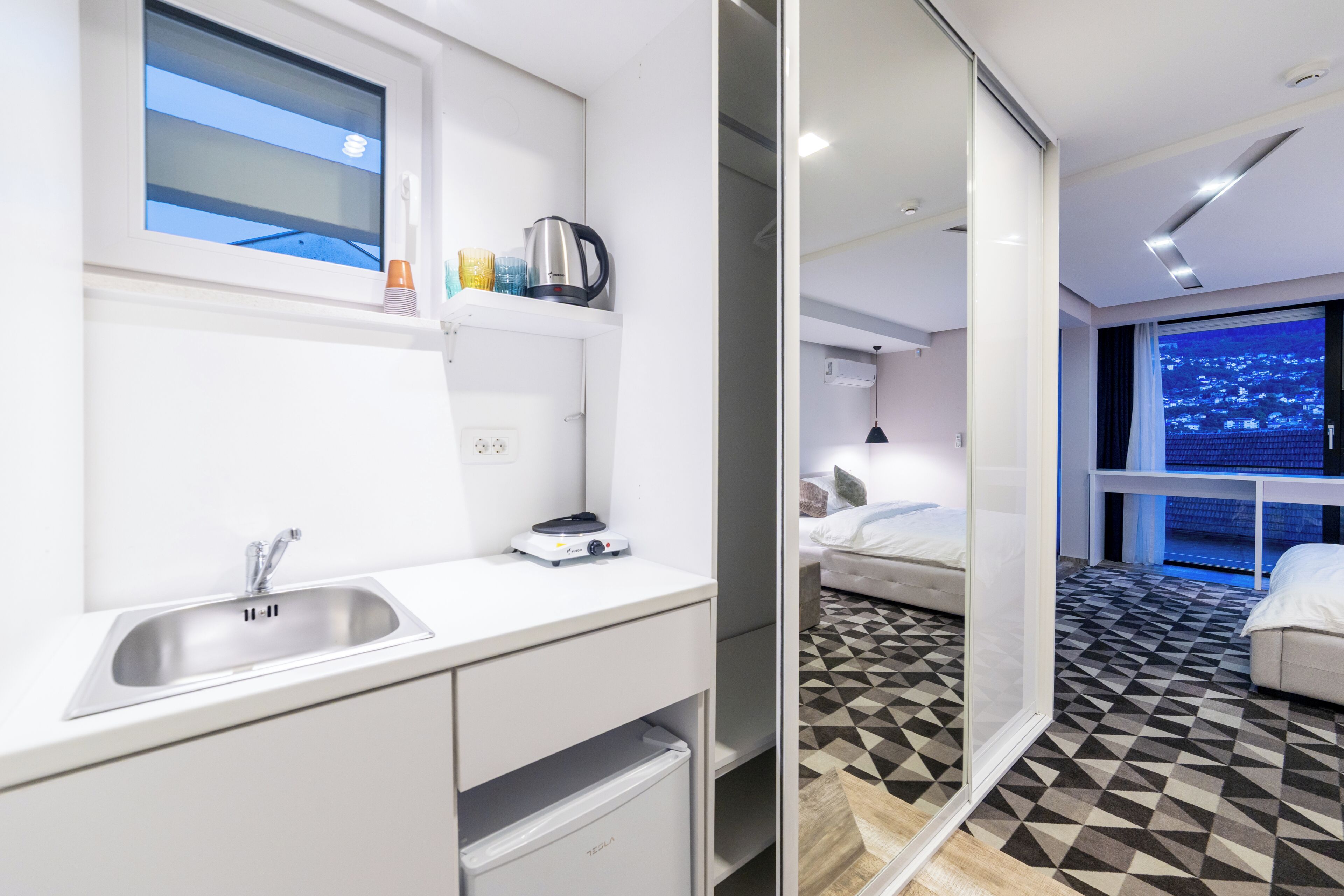 Una habitación de hotel moderna con cocina, cama y vistas a la ciudad.