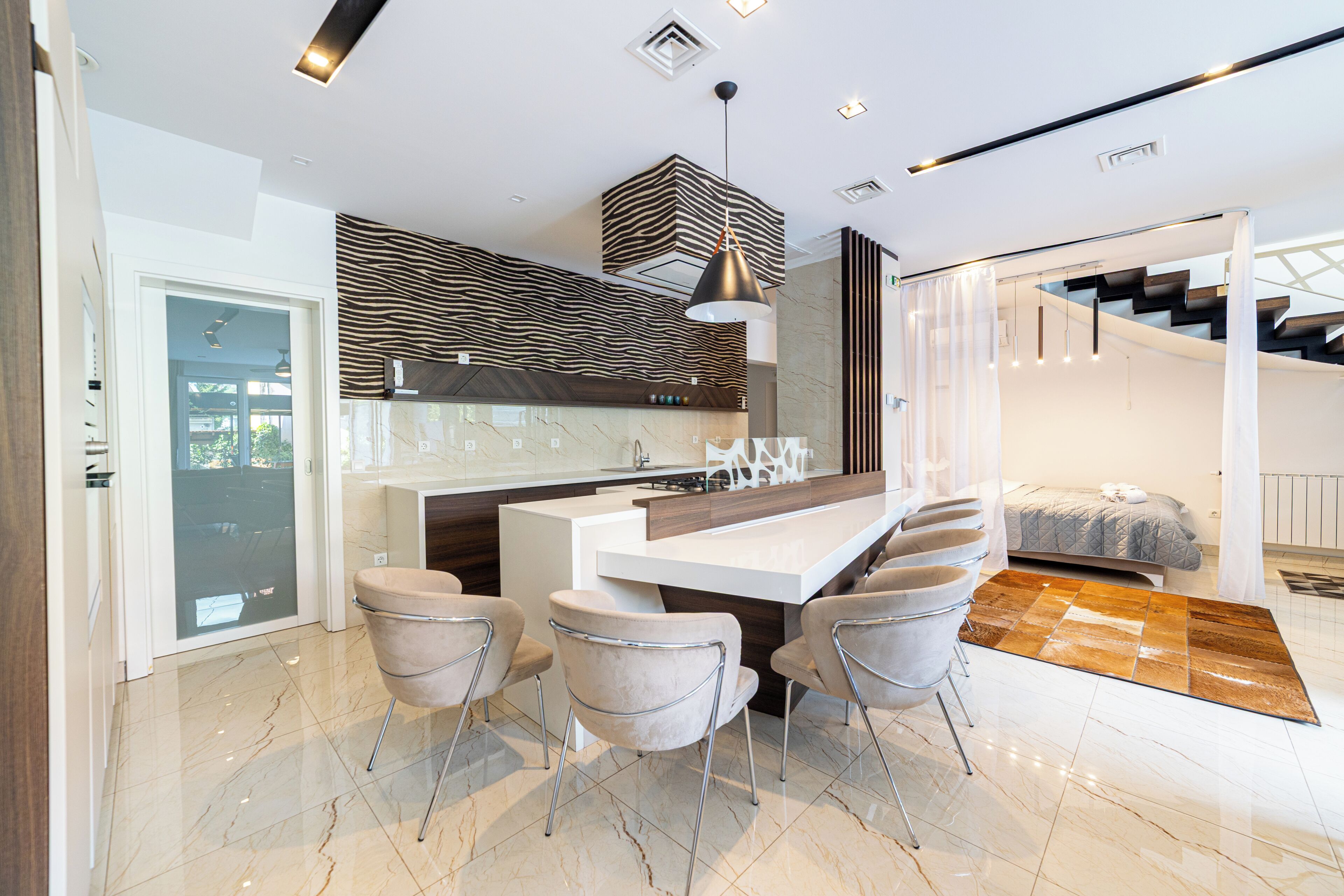 A modern kitchen with a central island, bar stools, and a staircase leading to an upper level.