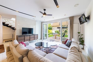 Ein modernes Wohnzimmer mit Sofa, Couchtisch, Fernseher und Deckenventilator.