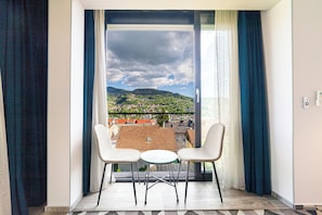 A balcony with two chairs and a small table, overlooking a cityscape with mountains. - Luxury Aparthotel MejtasHills - Old Town (Sarajevo)
