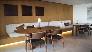 Un interior moderno con una mesa de comedor de madera, sillas, un sofá y una lámpara fijada a la pared.