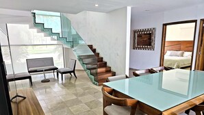 Ein modernes Interieur mit einer Glasstaircase, einem Essbereich mit Glastisch und einem Bett mit Holz Kopfteil.