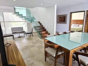 A modern interior with a glass staircase, a dining area with a glass table, and a bed with a wooden headboard. - Modern Villa · Private Pool · La Cruz Marina (Cruz de Huanacaxtle)