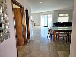 A spacious living area with a dining table, chairs, a sofa, and a kitchen area in the background.