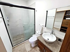 Une salle de bain avec une douche à parois de verre, des toilettes, un lavabo avec un miroir au-dessus et un meuble en bois.