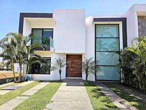 A modern two-story house with a large glass window, a wooden door, and a well-maintained lawn. - Modern Villa · Private Pool · La Cruz Marina (Cruz de Huanacaxtle)