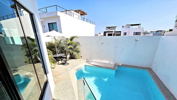 Ein modernes Gebäude mit Pool auf dem Dach, einer Glastür und einer Terrassenfläche mit Tisch und Stühlen.