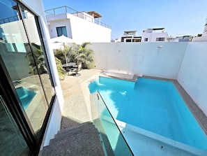 A modern building with a rooftop pool, a glass door, and a patio area with a table and chairs.