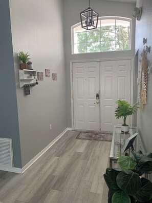 A hallway with a double door, a hanging light fixture, a small shelf with plants, and a wall-mounted sign. - Relaxing 3-Bedroom Vacation Home Relaxing Home with Pool, Golf & Tennis Sleeps 8 (Haines City)