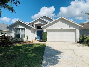 A residential house with a garage, a well-maintained lawn, and a clear blue sky. - Relaxing 3-Bedroom Vacation Home Relaxing Home with Pool, Golf & Tennis Sleeps 8 (Haines City)