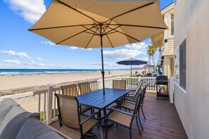 Una terraza con mesa y sillas, una parrilla y vista a la playa.