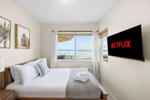 Habitación de hotel con una cama, un televisor en la pared y vista a la playa.