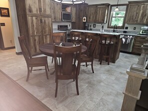Une cuisine avec des meubles en bois, un plan de travail en granit, une table à manger avec des chaises et un four encastré.
