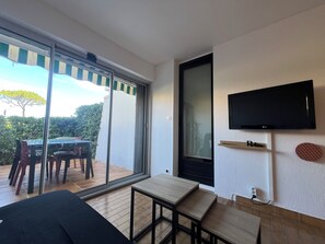 Une pièce dotée d’une porte-fenêtre coulissante donnant sur un espace extérieur, d’un téléviseur à écran plat fixé au mur et d’une petite table en bois.