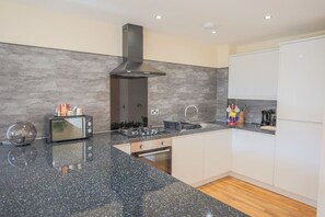 A modern kitchen with a granite countertop, a built-in oven, a stainless steel range hood, and white cabinetry. - Apartment in Edinburgh Newington (Edinburgh)