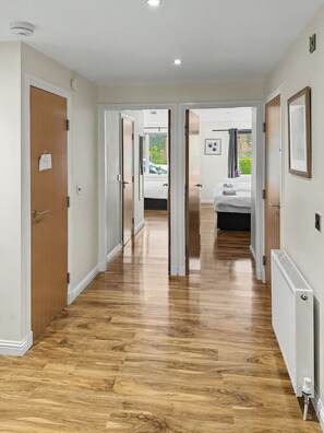 A hallway with wooden flooring, white walls, and doors leading to a bedroom with a bed and a window. - Apartment in Edinburgh Newington (Edinburgh)