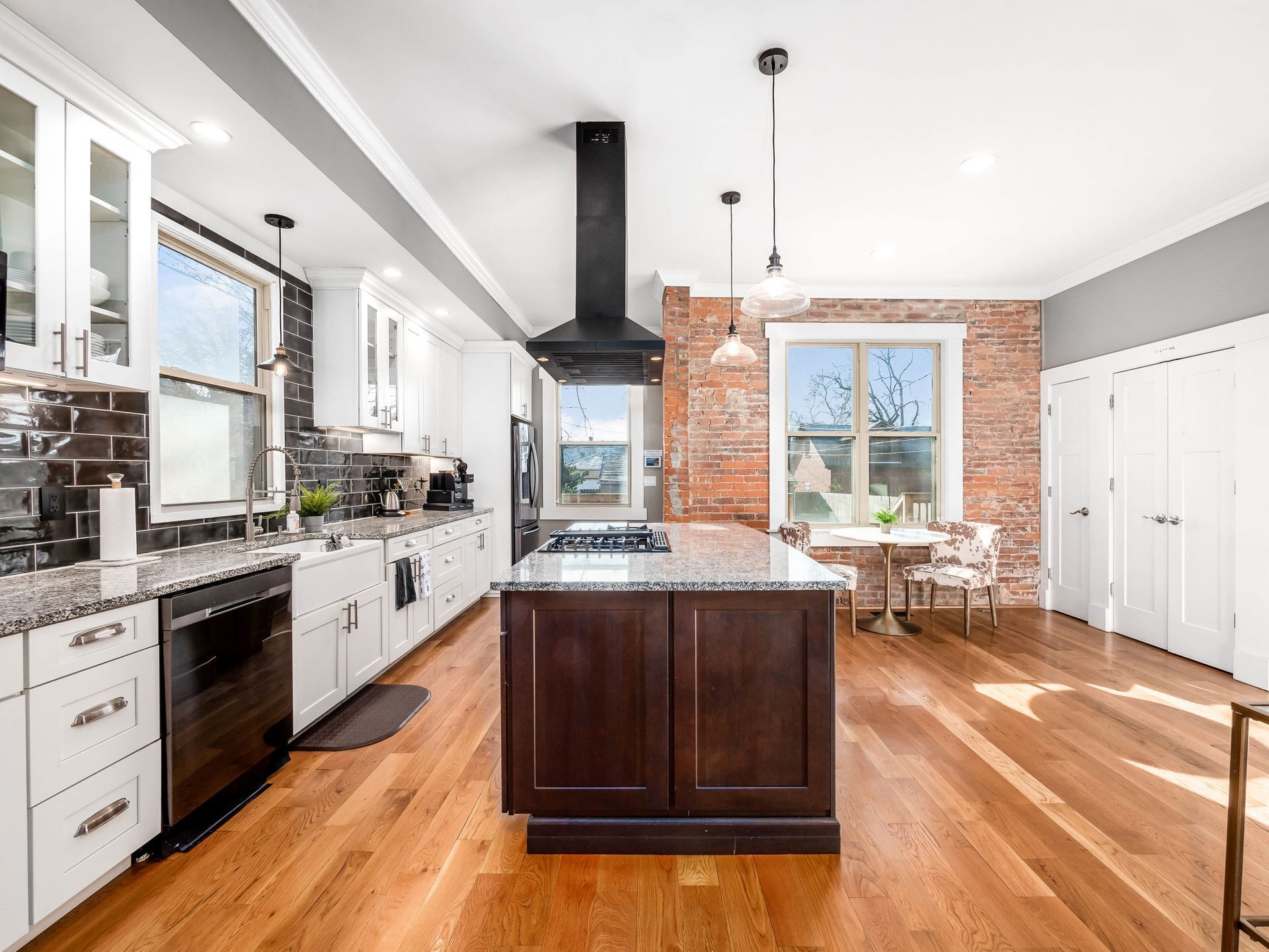 A modern kitchen with a central island, white cabinetry, a brick accent wall, and a dining area with a table and chairs.