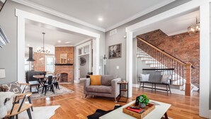 A spacious living area with a fireplace, a dining area, and a staircase with a brick wall. - Historic Home Near Downtown - Sleeps 14 - Arcade (Columbus)