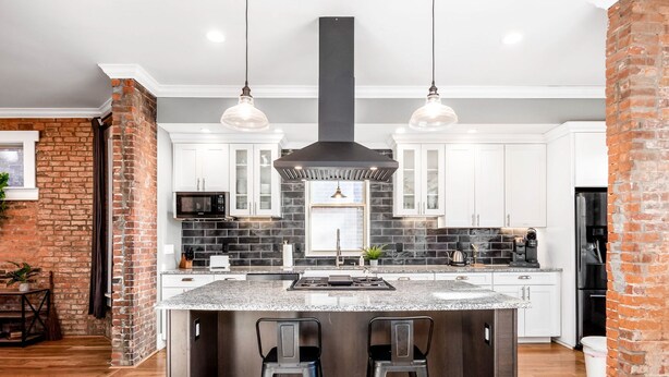 A modern kitchen with a central island, white cabinets, a black brick accent wall, and pendant lighting. - Historic Home Near Downtown - Sleeps 14 - Arcade (Columbus)