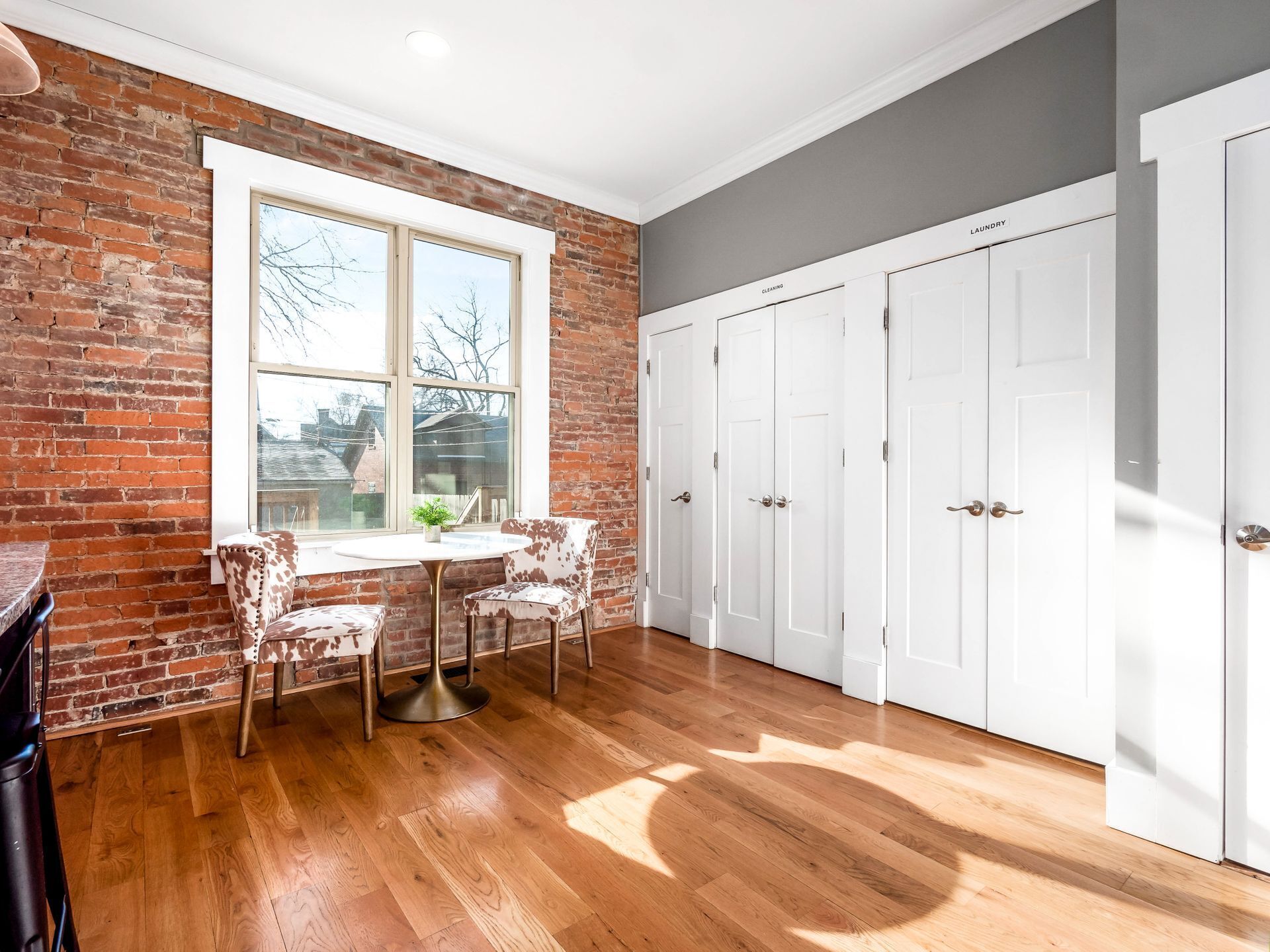 A room with a brick wall, a large window, a round table with chairs, and white doors labeled 'laundry' and 'cleaning.'