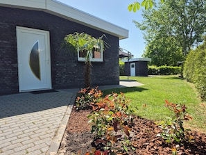 Un bâtiment moderne avec une porte blanche, un petit arbre et une pelouse bien entretenue.