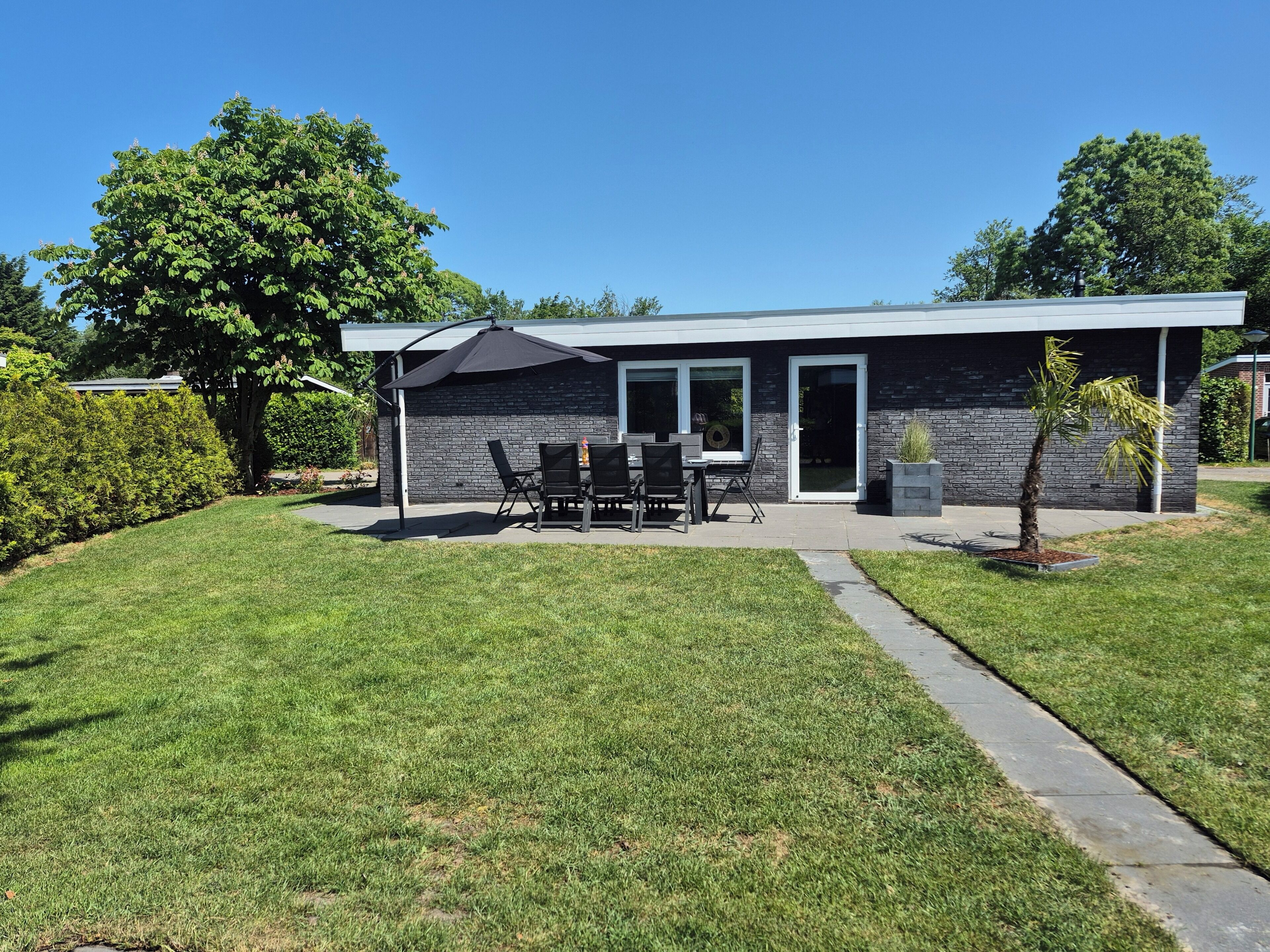 Een modern huis met terras, een eethoek en een kleine boom.