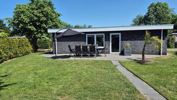 Een modern huis met terras, een eethoek en een kleine boom.