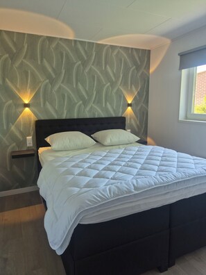 A bed with a quilted white duvet, a dark headboard, and two wall-mounted light fixtures.