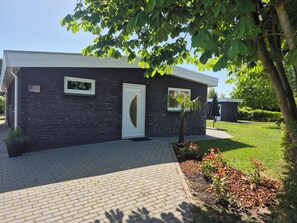 Un bâtiment moderne avec une façade en briques, une porte blanche et un petit arbre dans le jardin.