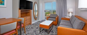 Une chambre d’hôtel équipée d’une télévision, d’un canapé, d’un fauteuil, d’une table, d’une commode et d’un balcon avec vue.