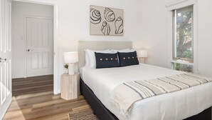 A bedroom with a bed, bedside lamps, a window, and a door. - Sunset Drift Edithvale Steps to Beach (Edithvale)