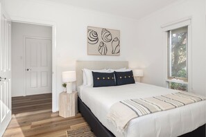 A bedroom with a bed, bedside lamps, a window, and a door.