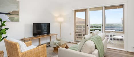 A modern living room with a television, a glass coffee table, a sofa, and a dining area with a table and chairs.