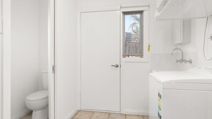 A small, white bathroom with a toilet, a window, and a sink. - Sunset Drift Edithvale Steps to Beach (Edithvale)