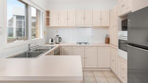 A modern kitchen with white cabinetry, a stainless steel sink, a gas stove, and a built-in oven. - Sunset Drift Edithvale Steps to Beach (Edithvale)