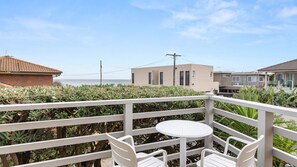 A balcony with a round table and two chairs, overlooking a residential area and the sea. - Sunset Drift Edithvale Steps to Beach (Edithvale)
