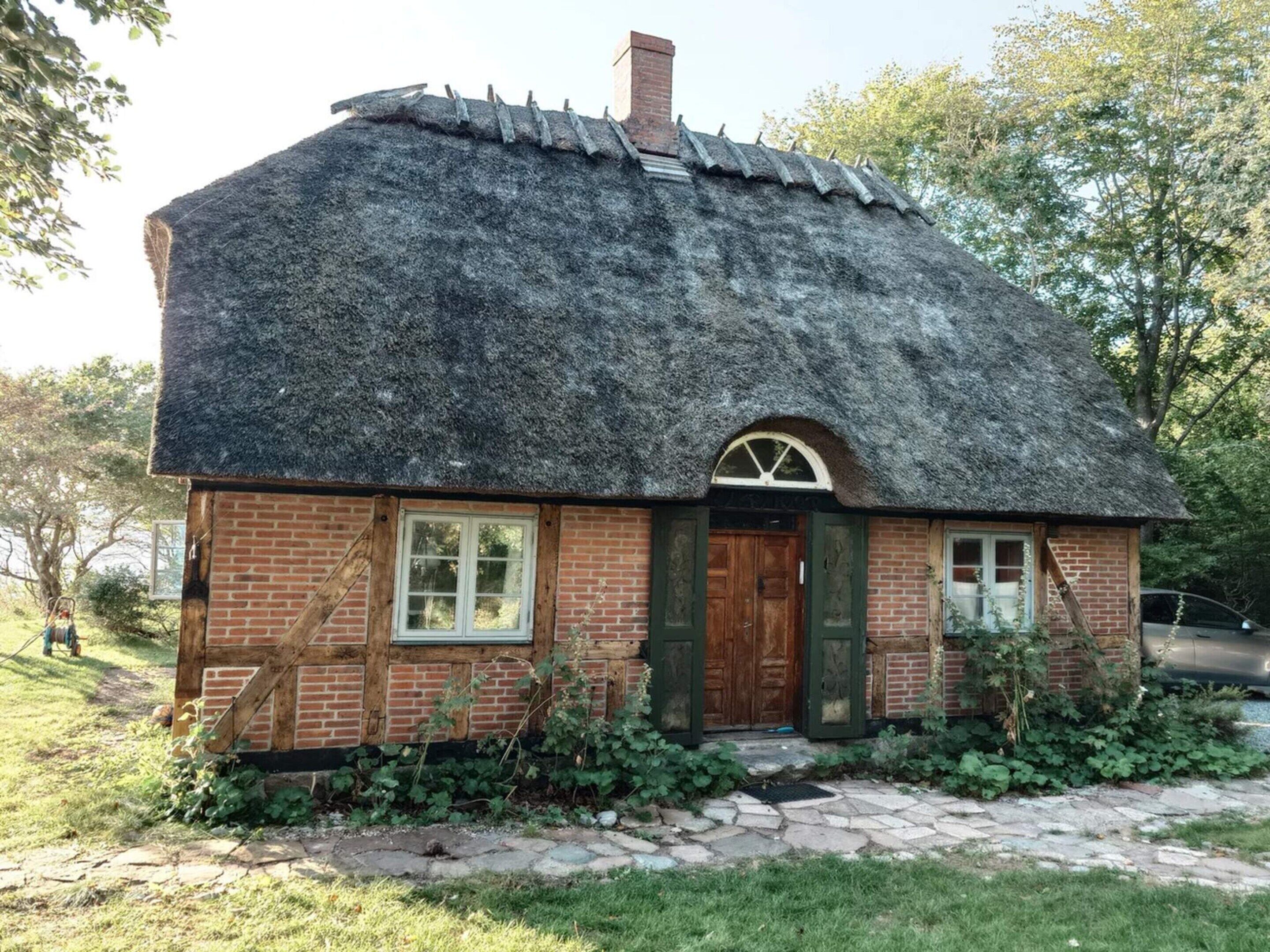 A small brick house with a thatched roof, a wooden door, and a stone pathway leading to the entrance.