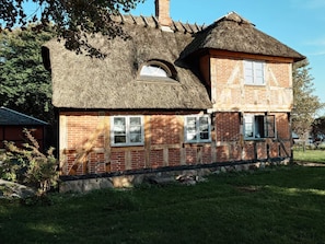 Ein traditionelles Backsteinhaus mit Strohdach und einem daran angebauten Nebengebäude.