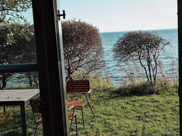 A view of a grassy area with a bench and a table, overlooking a body of water and trees. - 4 Star Holiday Home in Faaborg (Faaborg)