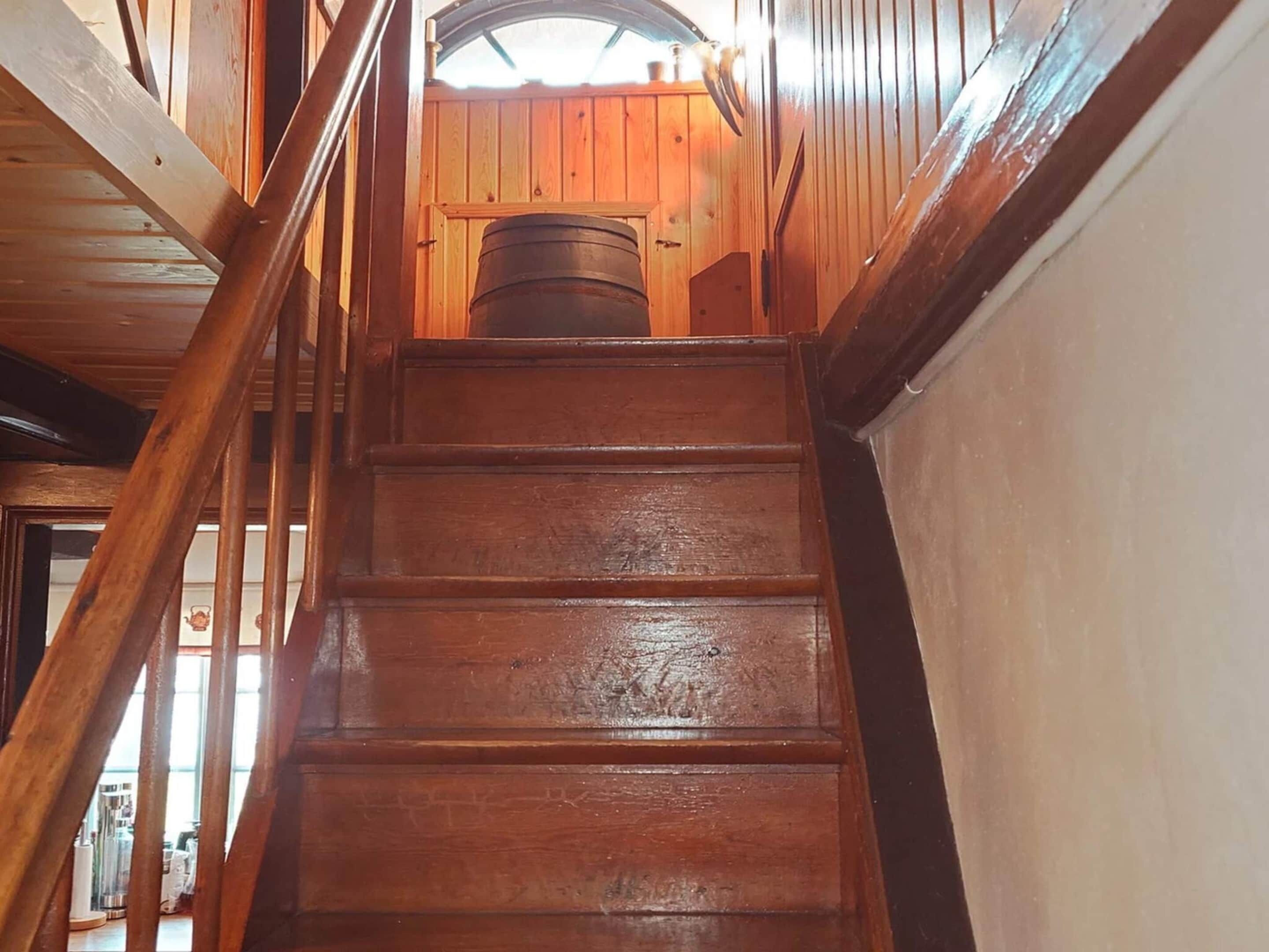 A wooden staircase with a metal barrel in the background.