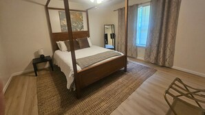 Una cama con dosel, un ventilador de techo, una mesita de noche, un espejo y una ventana con cortinas.