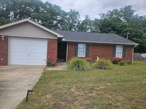 A single-story brick house with a garage, a front door, and a small front yard with landscaping.