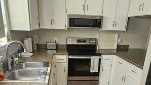 Una cocina con armarios blancos, electrodomésticos de acero inoxidable, encimera de granito y piso de madera.