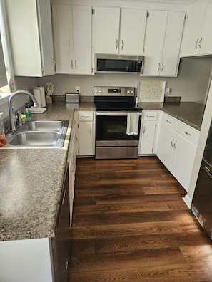A kitchen with white cabinets, stainless steel appliances, a granite countertop, and a wooden floor.