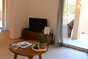 A living room with a television, a coffee table with magazines and a plant, and a view of the outdoors through a glass door. - A heavenly spot in gigaro, 5min from pl6 (La Croix-Valmer)