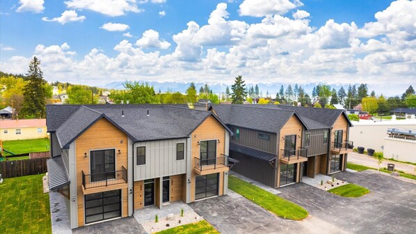 A row of modern, two-story townhouses with attached garages, set against a backdrop of mountains and a clear sky.