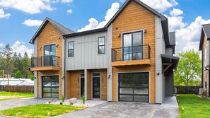 A two-story house with a modern design, featuring a combination of wooden and grey siding, large windows, and a balcony on the upper floor.