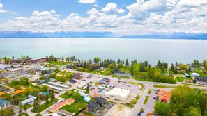 An aerial view of a lakeside town with buildings, roads, and a clear view of the lake and mountains in the background.