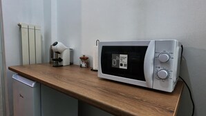 Un microondas sobre una encimera de madera, con una pared blanca y un radiador al fondo.
